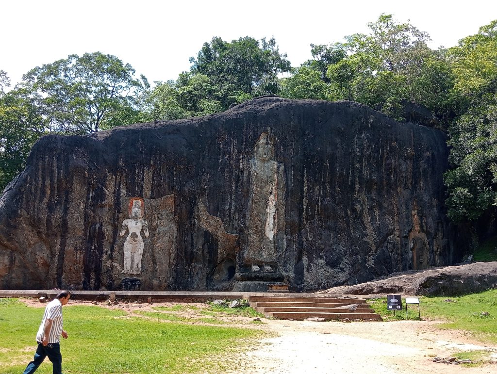 Seven huge Buddha statues hewn out of a sheer cliff side in a quiet green clearing